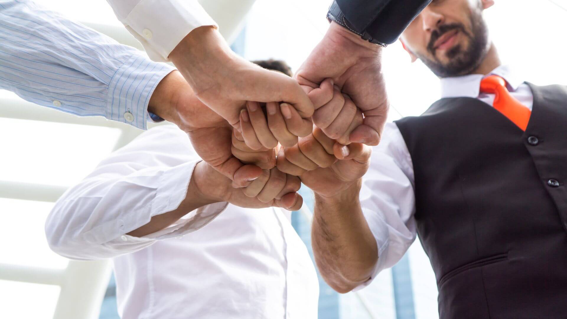 business team of five doing fist pump as unity, with hands in centre